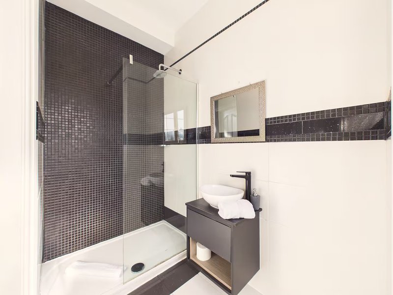 Modern bathroom with walk-in shower, dark tile, white sink and mirror