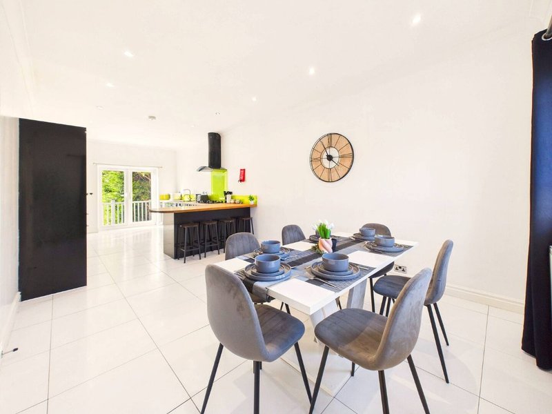Open-plan dining and kitchen area with white tile floor, dining table set for four, and kitchen counter in background