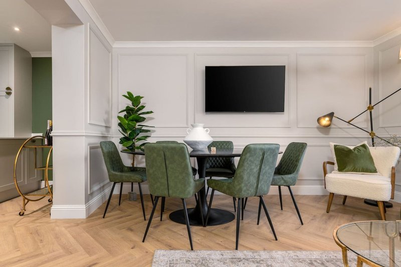Modern dining room with round black table, green upholstered chairs, wall-mounted TV and herringbone flooring