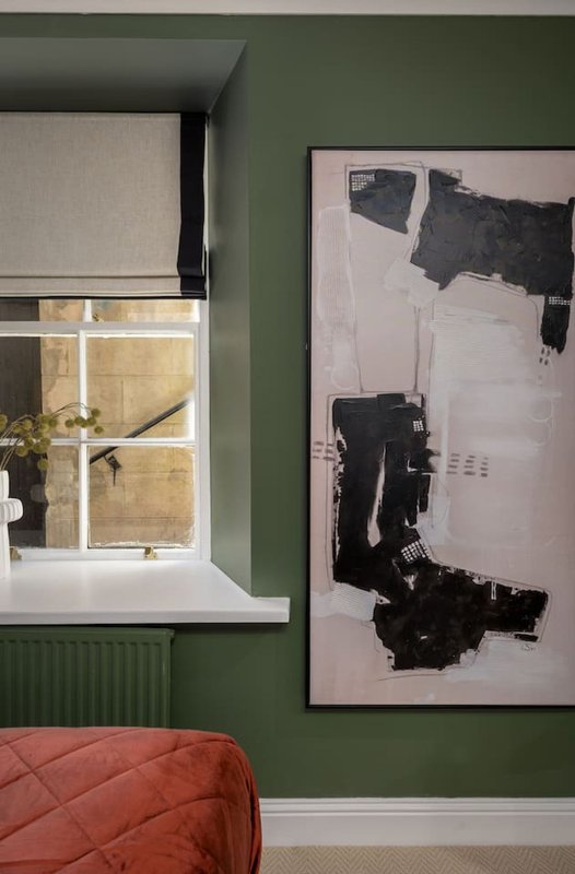 Green bedroom wall with window, radiator, abstract framed artwork and red upholstered chair