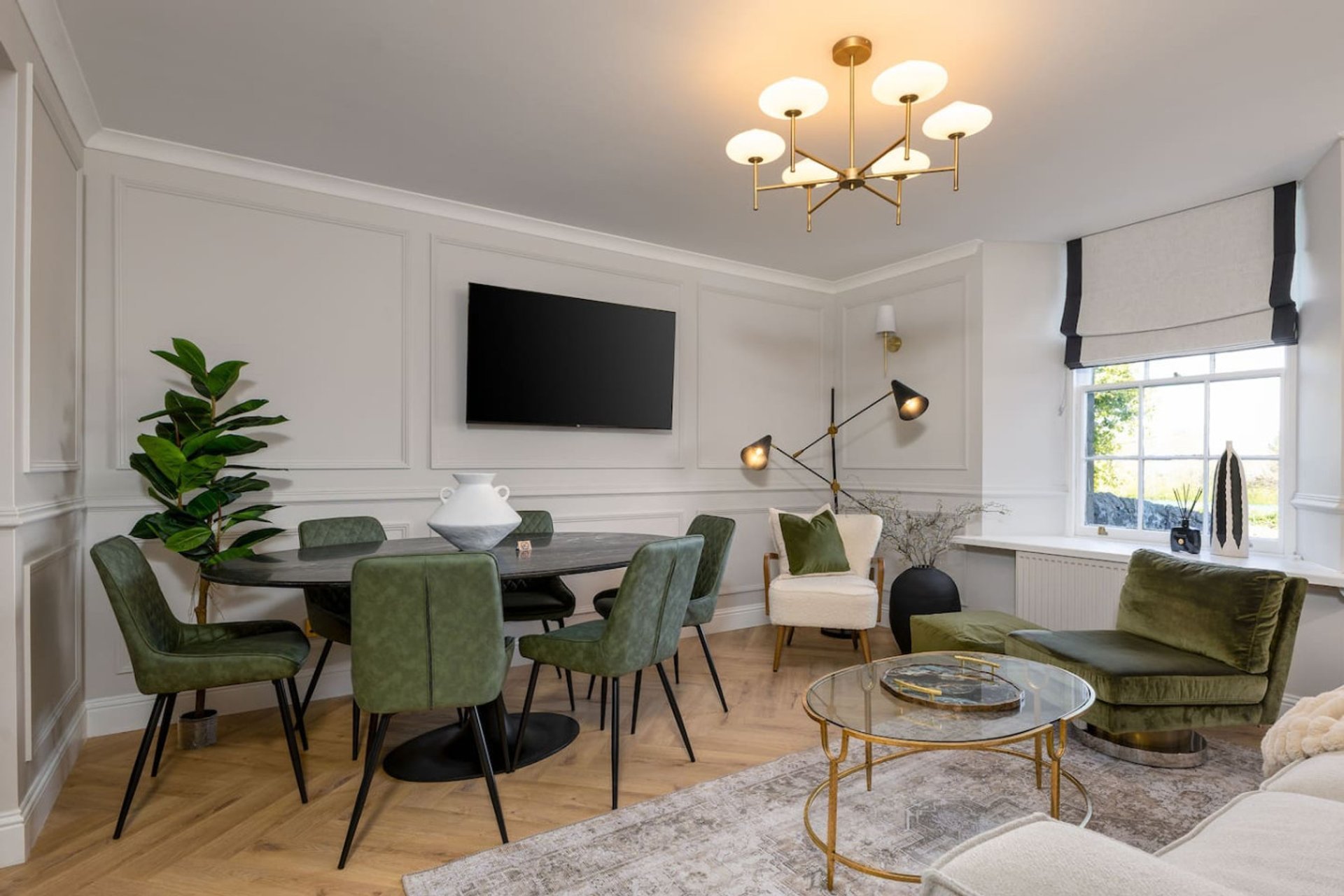Open-plan living and dining area with green upholstered chairs, round table, TV, and modern ceiling light