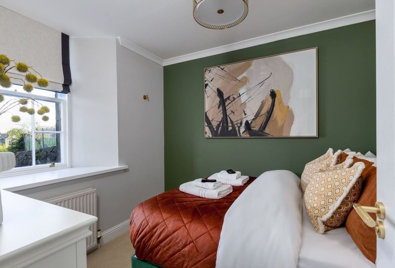 Modern bedroom with green accent wall, double bed, framed artwork, and window with blinds
