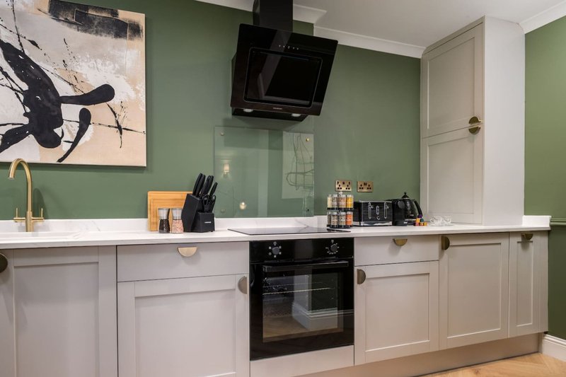 Modern kitchen with white cabinetry, green walls, black appliances and countertop accessories