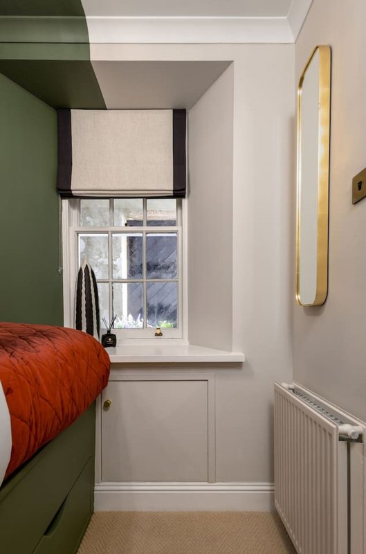 Bedroom with green feature wall, single bed with red bedding, window with blind, and wall-mounted mirror