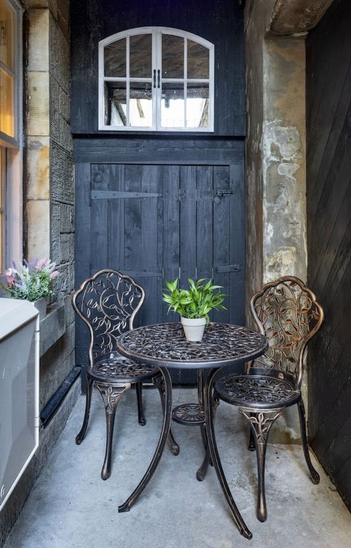 Narrow courtyard with dark blue door, small round table, two ornate chairs and potted plant
