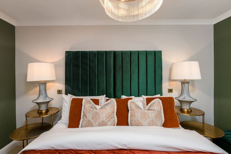 Modern bedroom with green upholstered headboard, white bedding, decorative pillows and brass lamps