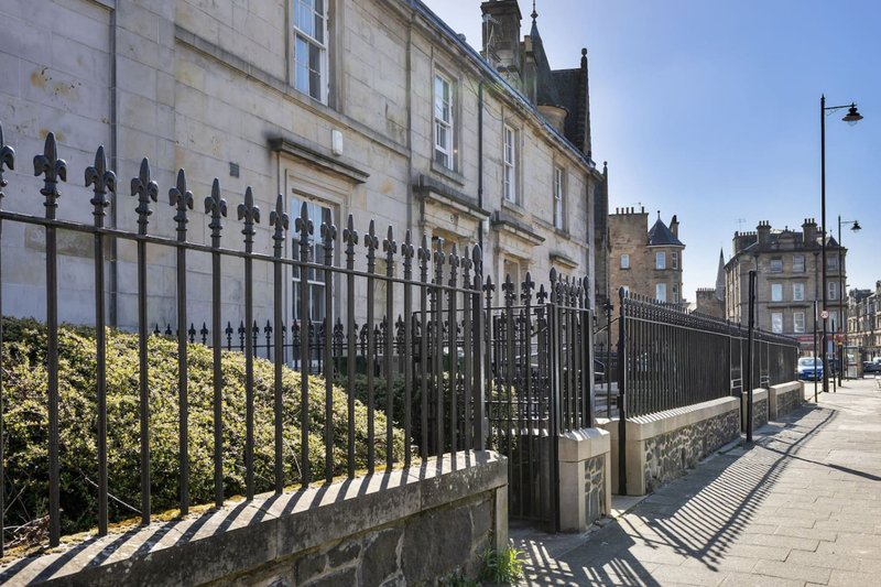Street view of traditional stone buildings with black iron railings and manicured hedges