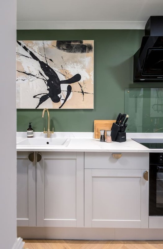 Modern kitchen with white cabinetry, green wall, framed abstract artwork, and stainless steel sink