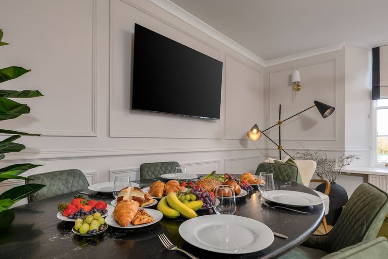 Modern dining room with black table, place settings, fruit display, wall-mounted TV and pendant lighting