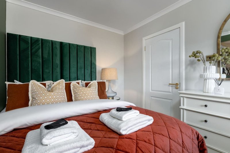 Modern bedroom with green velvet headboard, red quilted bedspread, and white furnishings