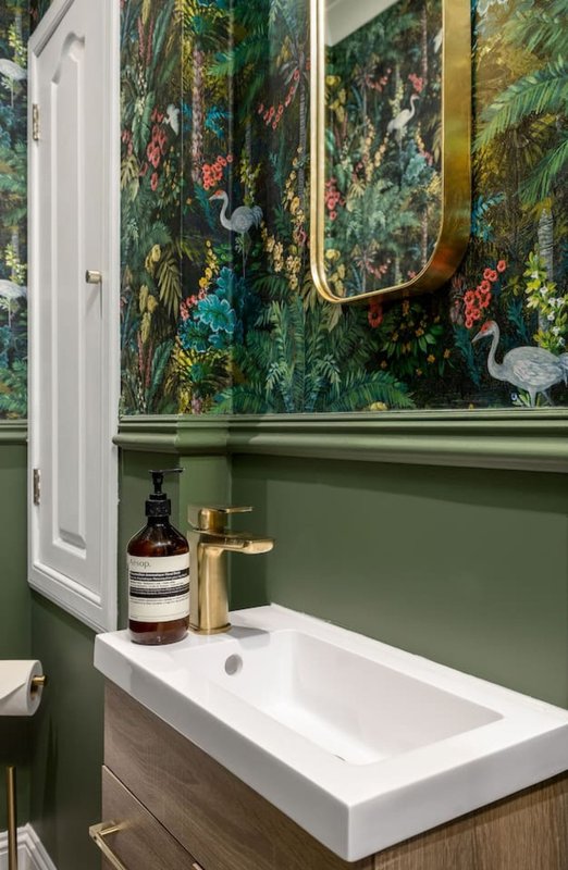Bathroom sink with green wall paneling, floral wallpaper, and brass fixtures