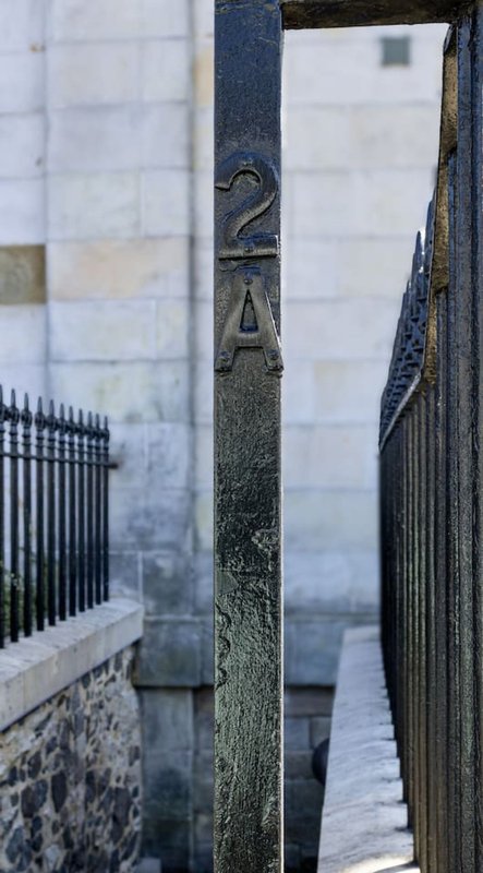 Narrow alleyway between stone buildings with black iron railings and wooden gate