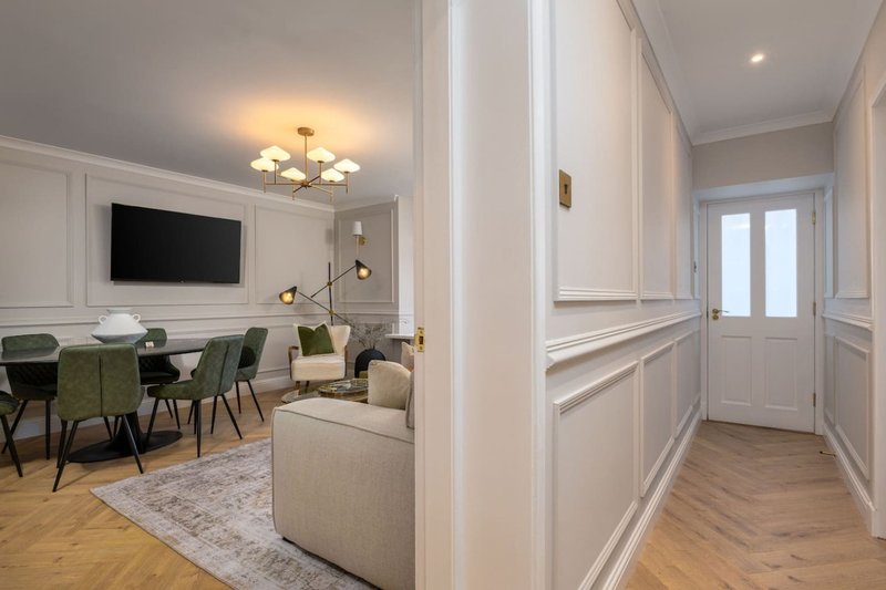 Modern living room with cream sofa, dining table, wall-mounted TV, and hallway entrance