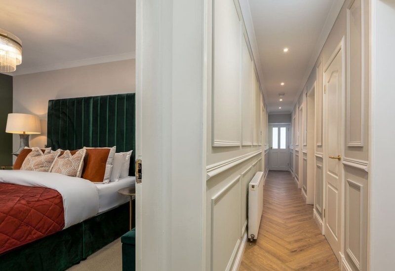 Bedroom with green upholstered headboard and hallway with white panelled doors