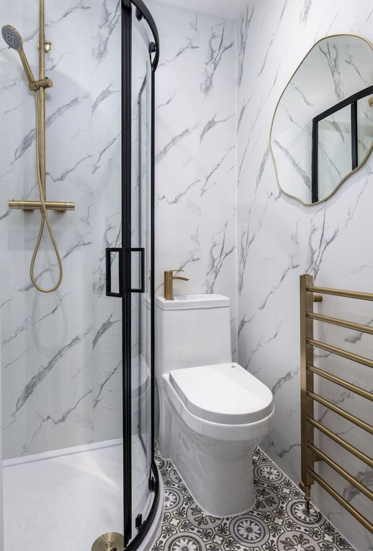 Modern bathroom with marble-look tile walls, black-framed shower enclosure, white toilet, and brass fixtures