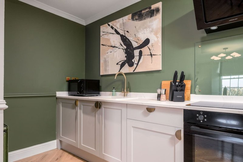 Modern kitchen with sage green walls, white cabinetry, and black appliances