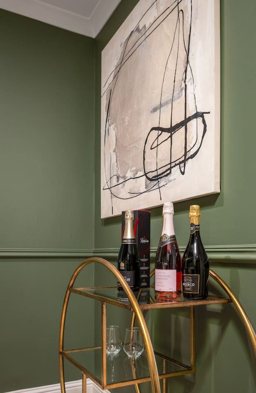 Corner display with wine bottles, glasses, and abstract line art print on green wall