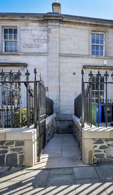 Stone townhouse entrance with black iron railings, blue wheelie bin, and symmetrical windows