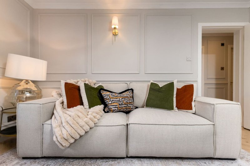 Modern living room with light gray sectional sofa, decorative pillows, throw blanket, and wall sconce lighting