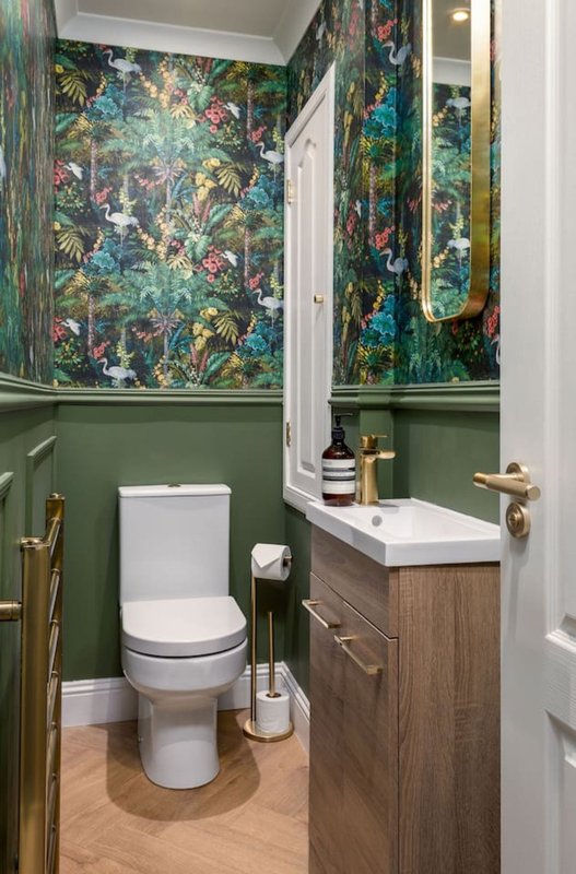 Modern bathroom with green paneling, patterned wallpaper, white toilet, wooden vanity and sink