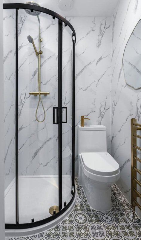 Modern bathroom with curved black-framed shower enclosure, white toilet, and marble-look wall tiles