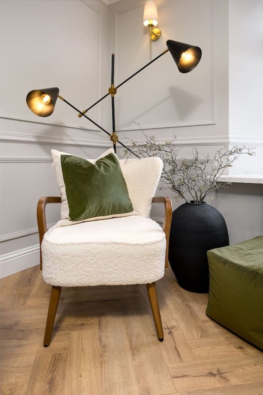 Modern living room with cream armchair, green cushion, brass pendant light, and wooden flooring