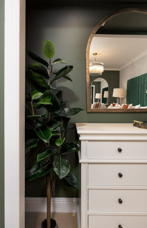 Bathroom vanity with white drawers, round mirror, potted plant and dark wall