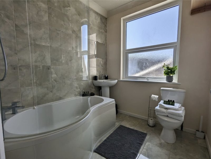 Modern bathroom with corner bathtub, toilet, pedestal sink, and large window overlooking landscape