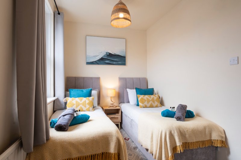 Twin bedroom with two single beds, blue and gold cushions, bedside lamps and framed landscape artwork