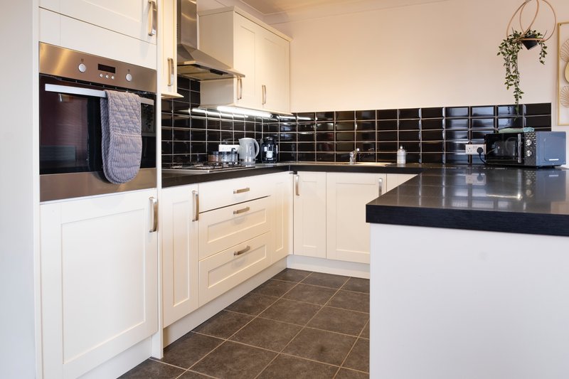 Modern kitchen with white cabinetry, black tile backsplash, dark countertops and built-in oven