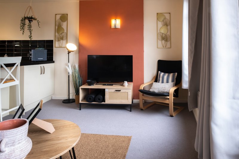 Open-plan living area with kitchenette, TV, wooden furniture, and orange accent wall