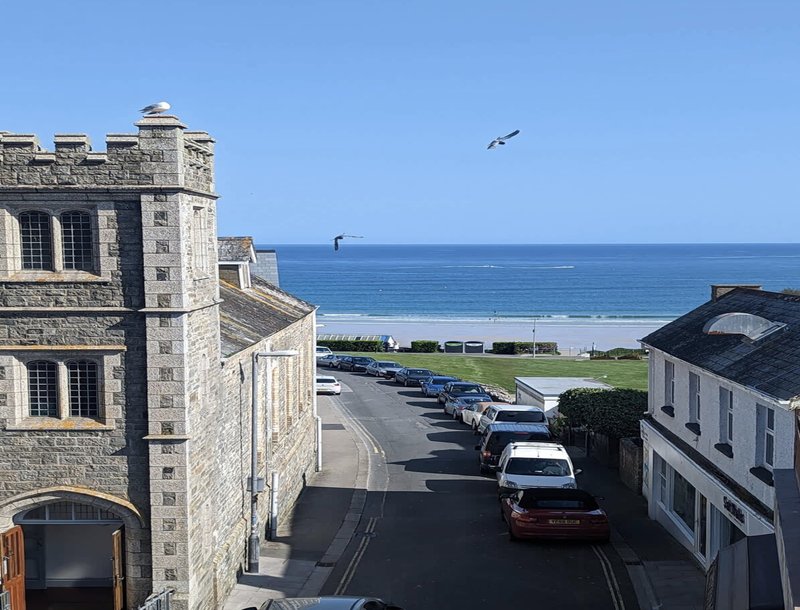 Coastal street view with stone buildings, parked cars, beach and sea in background