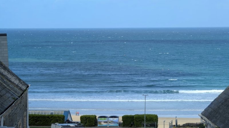 Coastal beach view with ocean waves, sand, and residential properties in foreground