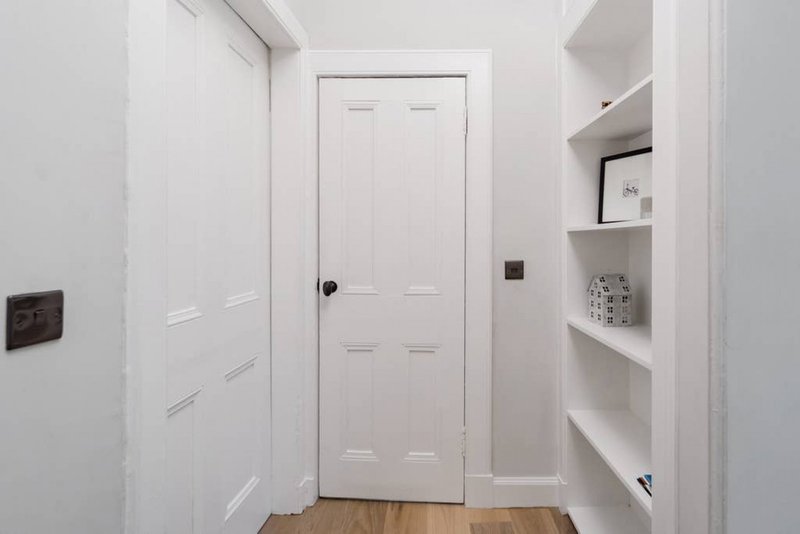 White hallway with built-in shelving, wooden floor and interior doors