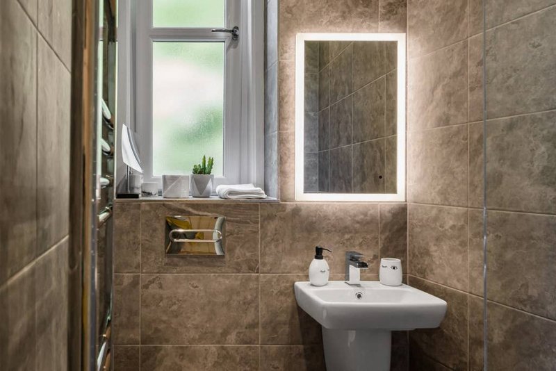 Modern bathroom with tiled walls, illuminated mirror, window and pedestal sink