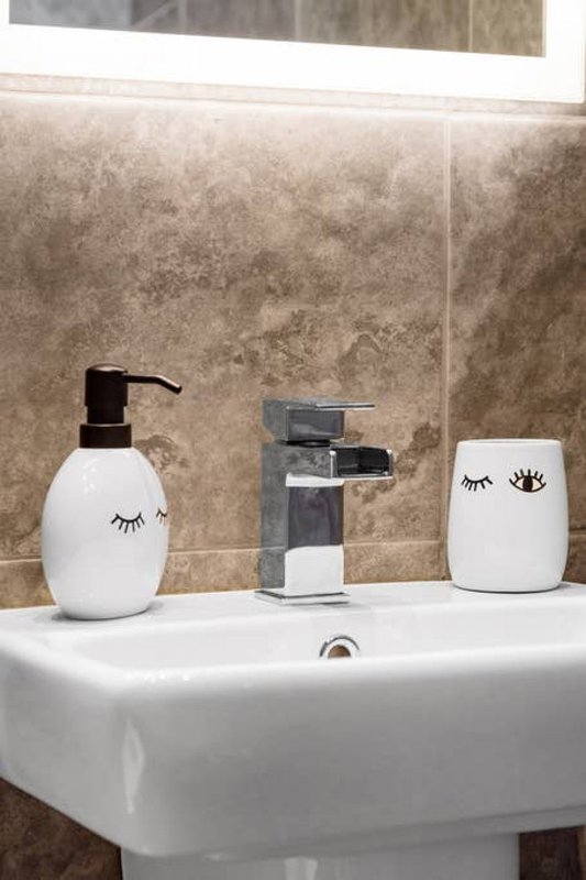 Bathroom sink with chrome faucet, soap dispenser, and decorative white containers with eyelash designs