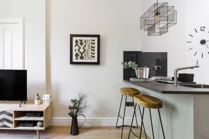 Modern living room with kitchen counter, wooden stools, framed wall art, and minimalist decor