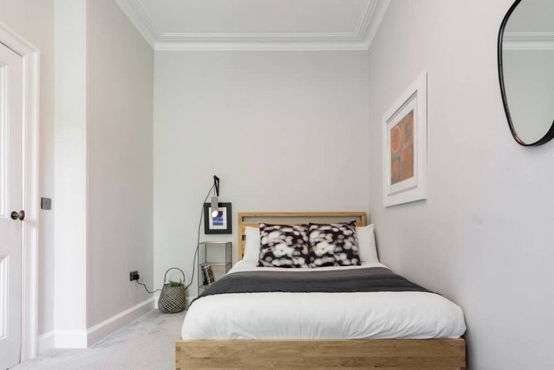 Bright bedroom with wooden bed frame, white bedding, patterned pillows and wall art