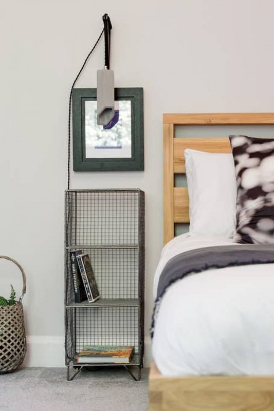 Bedroom corner with wooden bed frame, white pillows, patterned throw, wall-mounted organizer and metal storage unit