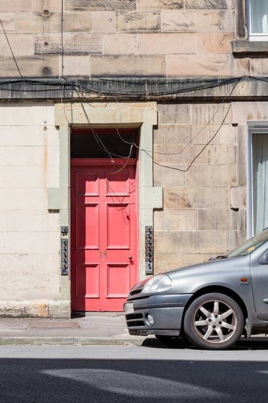Stone building exterior with bright red door and parked car on street