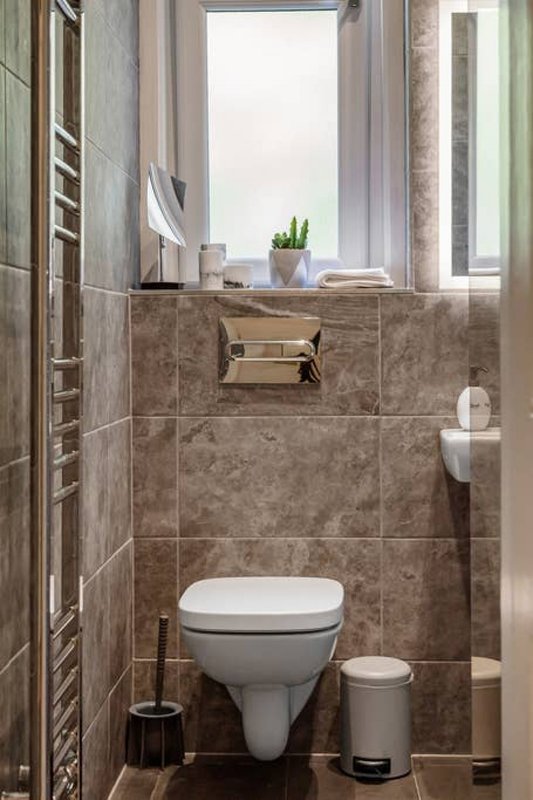 Compact bathroom with wall-mounted toilet, tiled walls, window with sill decor, and heated towel rail