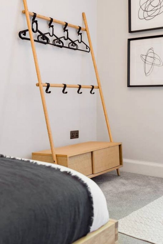 Modern wooden coat rack with hooks and storage bench against white wall with framed artwork