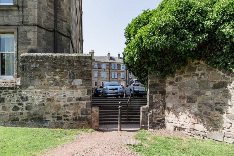 Stone building exterior with driveway, metal gate, ivy-covered wall and parked cars
