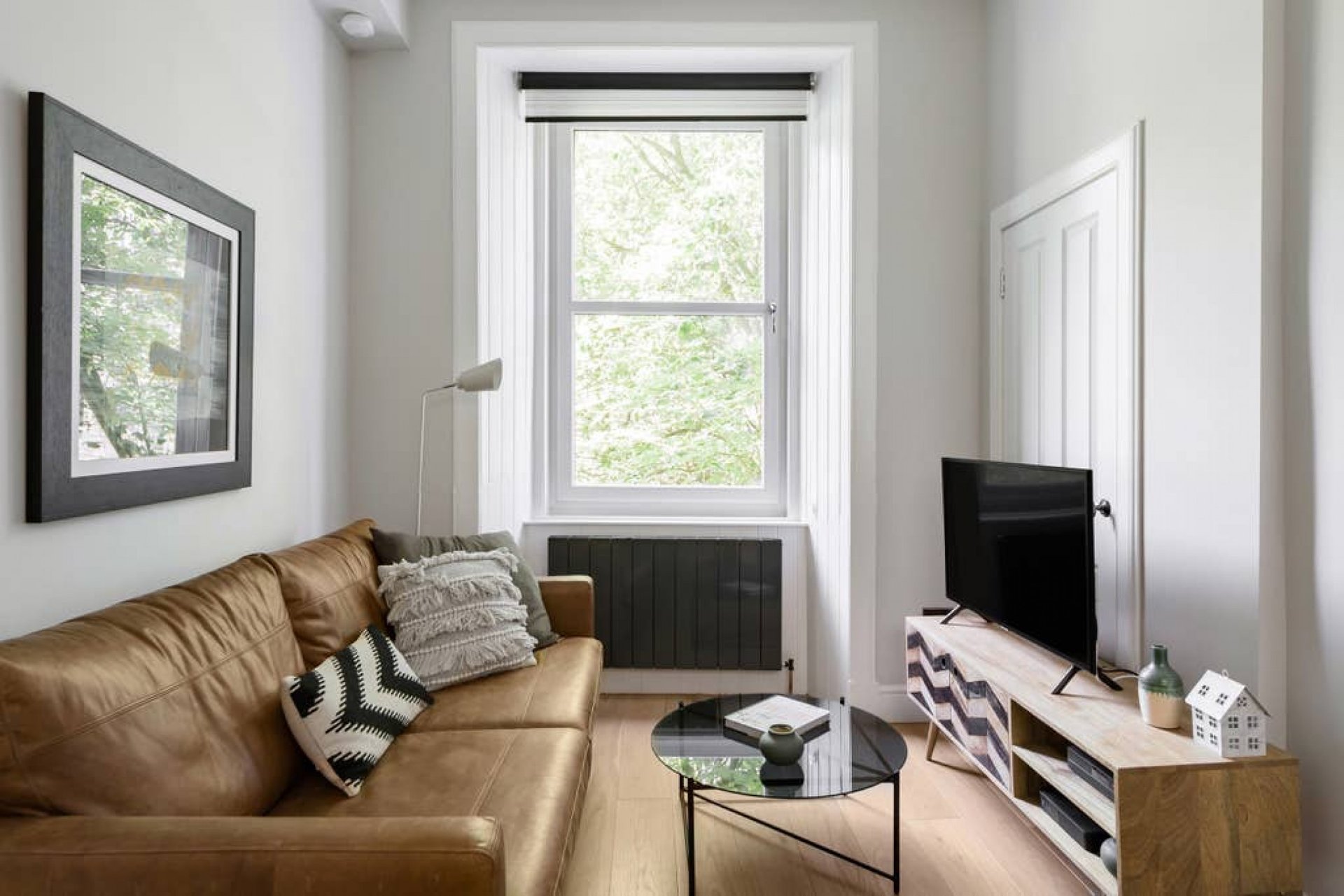 Living room with tan leather sofa, TV on stand, windows, and modern furnishings