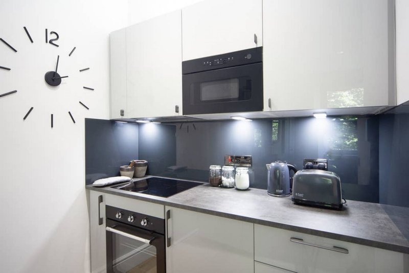 Modern kitchen with white cabinetry, dark backsplash, stainless steel appliances and wall clock