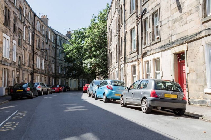 Street view of parked cars between traditional stone tenement buildings with trees