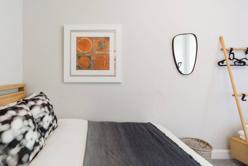 Modern bedroom with double bed, framed artwork, mirror, and wooden shelving unit