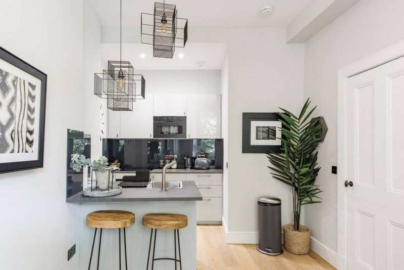 Modern kitchen with black countertop, wooden bar stools, pendant lights, and potted plant