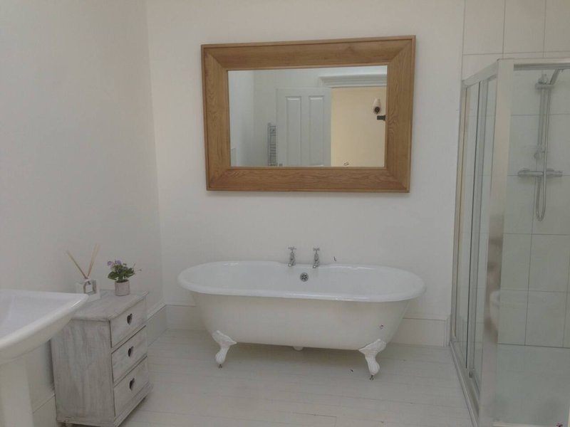 Bathroom with freestanding white bathtub, wooden-framed mirror, and shower enclosure