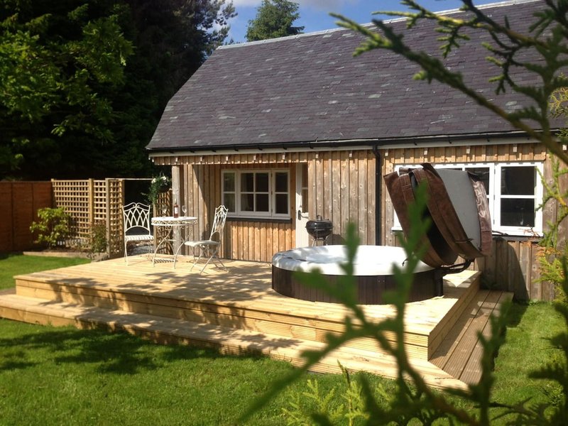Wooden garden building with decking, seating area, hot tub and manicured lawn